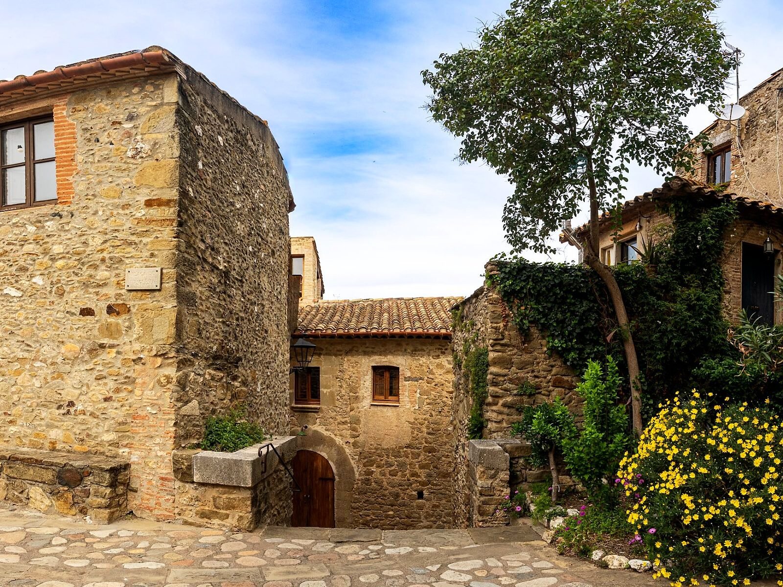 Casas rústicas de piedra y calles empedradas rodeadas de flora exuberante.